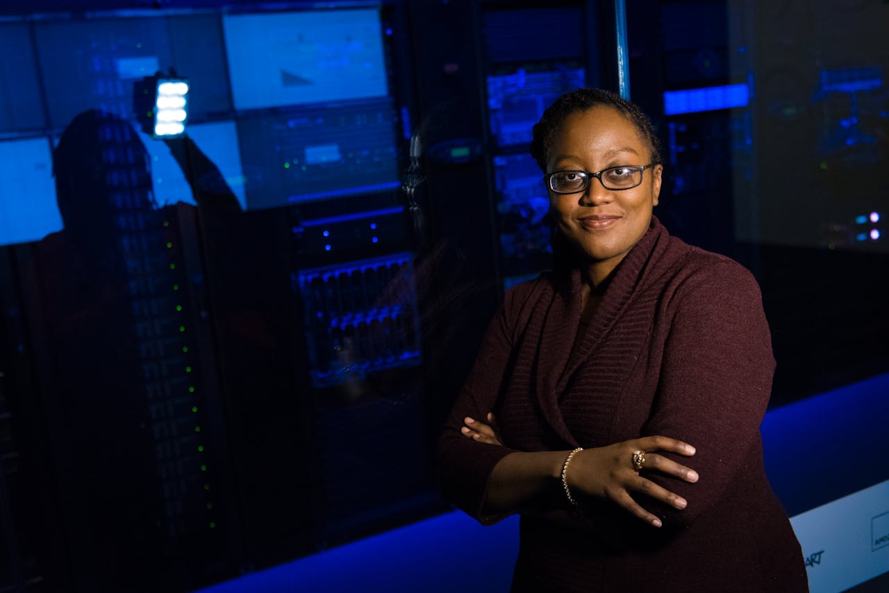 our-story-01 Professional woman standing confidently in a data center, surrounded by glowing servers.
